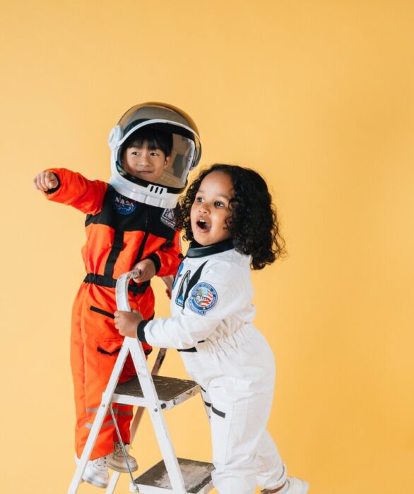 Kinder spielen als Astronauten verkleidet auf einer Leiter.